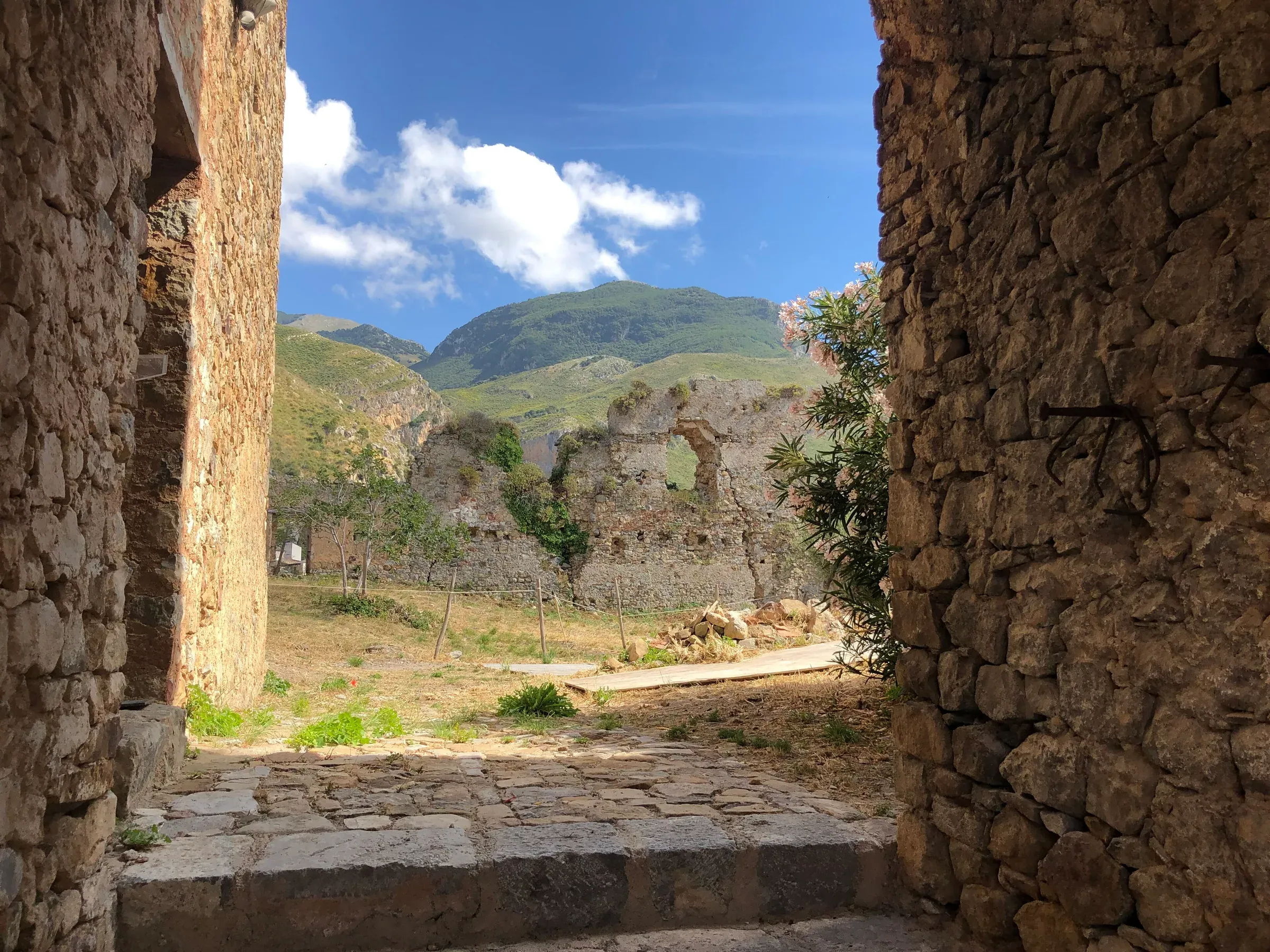 I ruderi del castello di Collesano visti da un passaggio tra muri di pietra, con le montagne verdi delle Madonie sullo sfondo