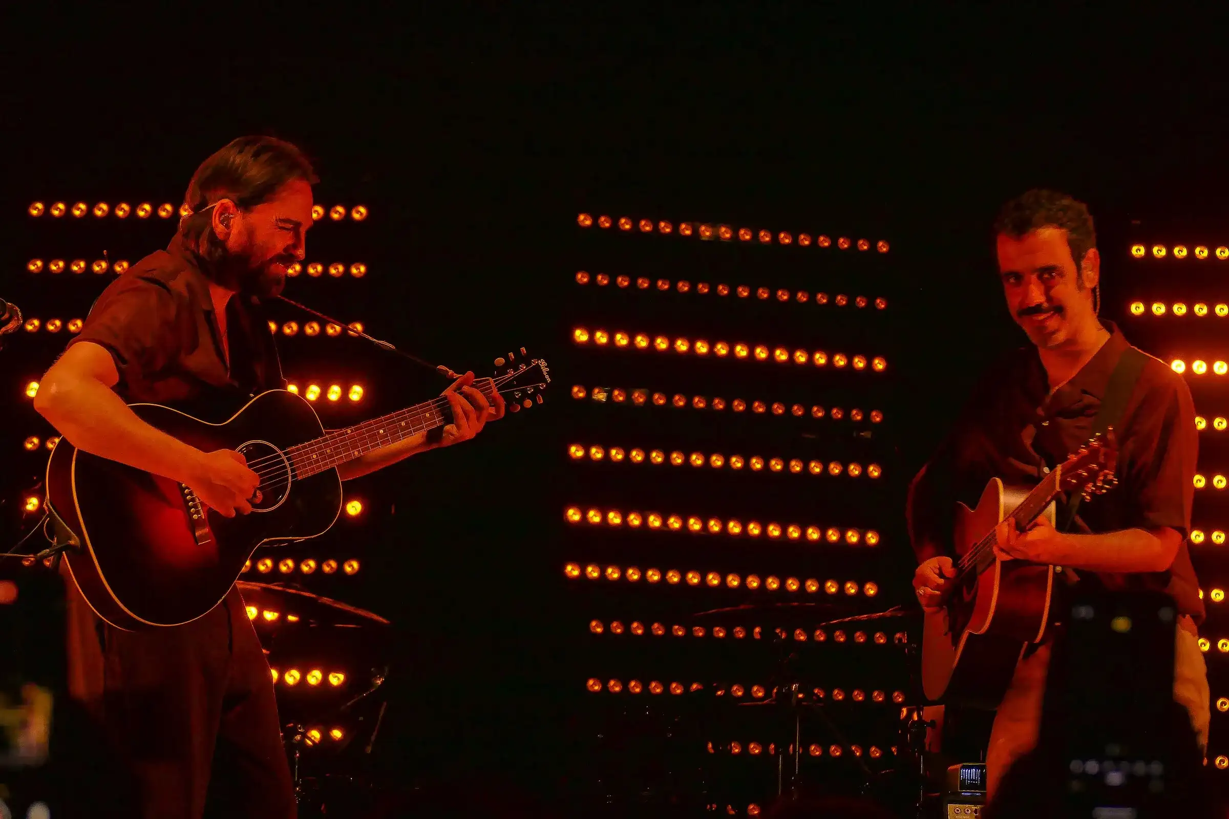 Colapesce e Dimartino suonano la chitarra sul palco dell’Ypsigrock Festival 2024 a Castelbuono, tra le luci arancioni