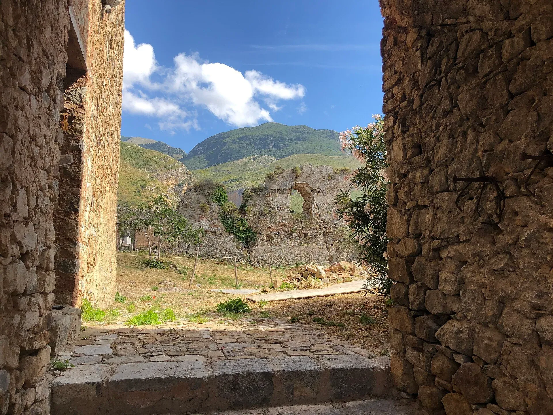 I ruderi del castello di Collesano visti da un passaggio in pietra, con i monti verdi dietro
