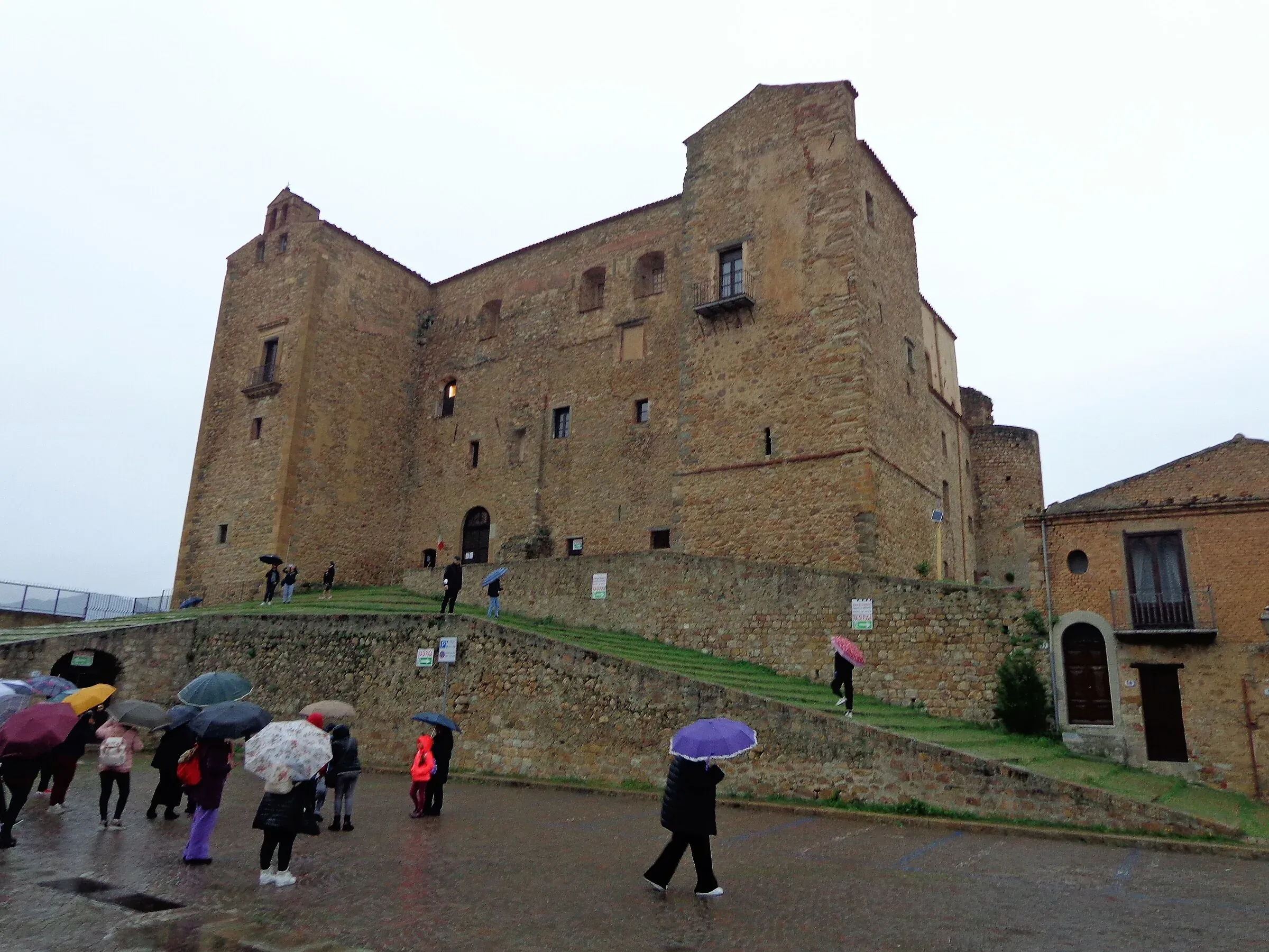Il castello dei Ventimiglia a Castelbuono in una giornata di pioggia, con i visitatori sotto gli ombrelli in Piazza Castello