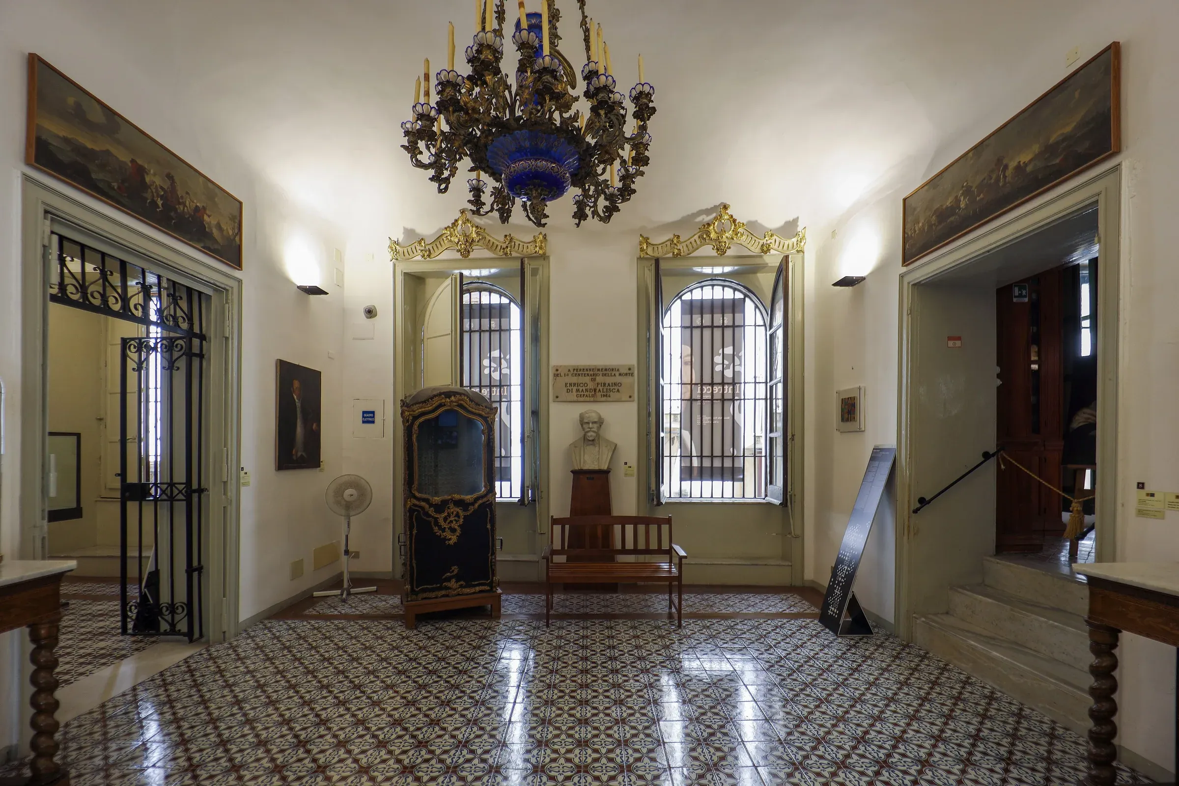 Una sala del Museo Mandralisca di Cefalù con il busto del barone, una portantina dorata e un lampadario di vetro blu