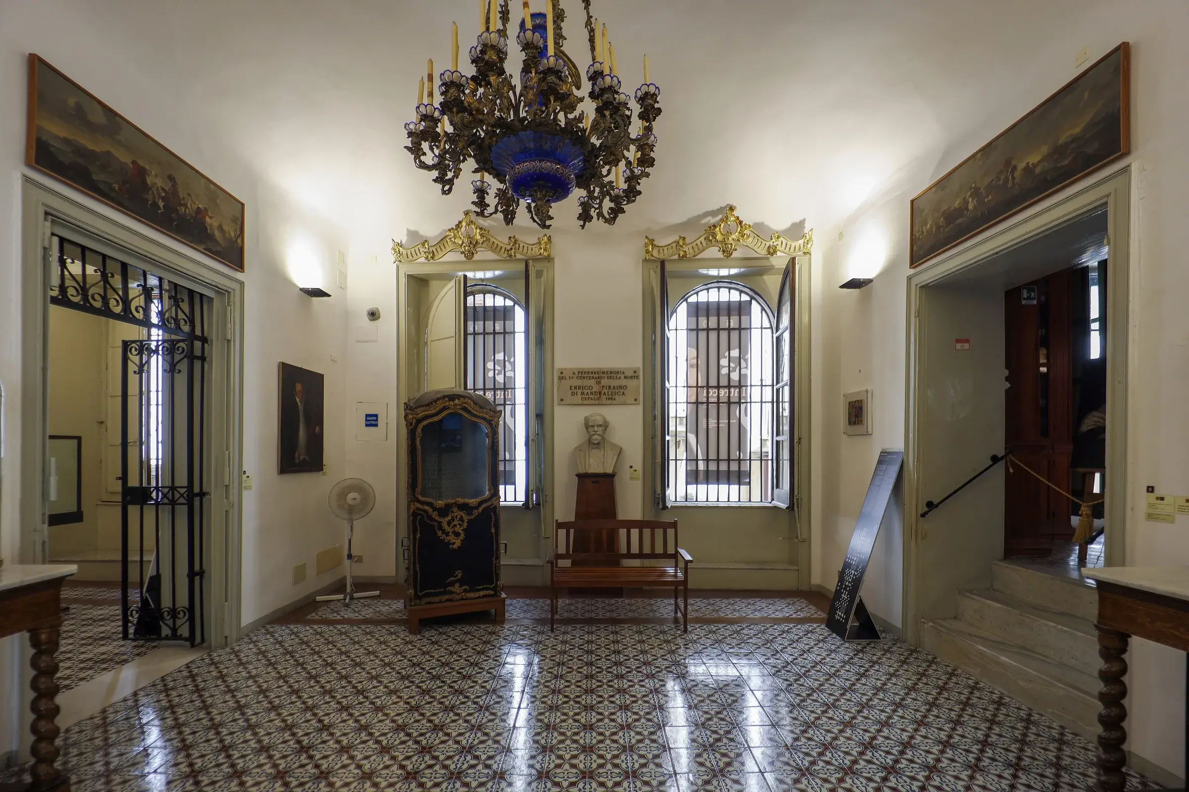 Una sala del Museo Mandralisca di Cefalù con il busto del barone, una portantina dorata e un lampadario di vetro blu