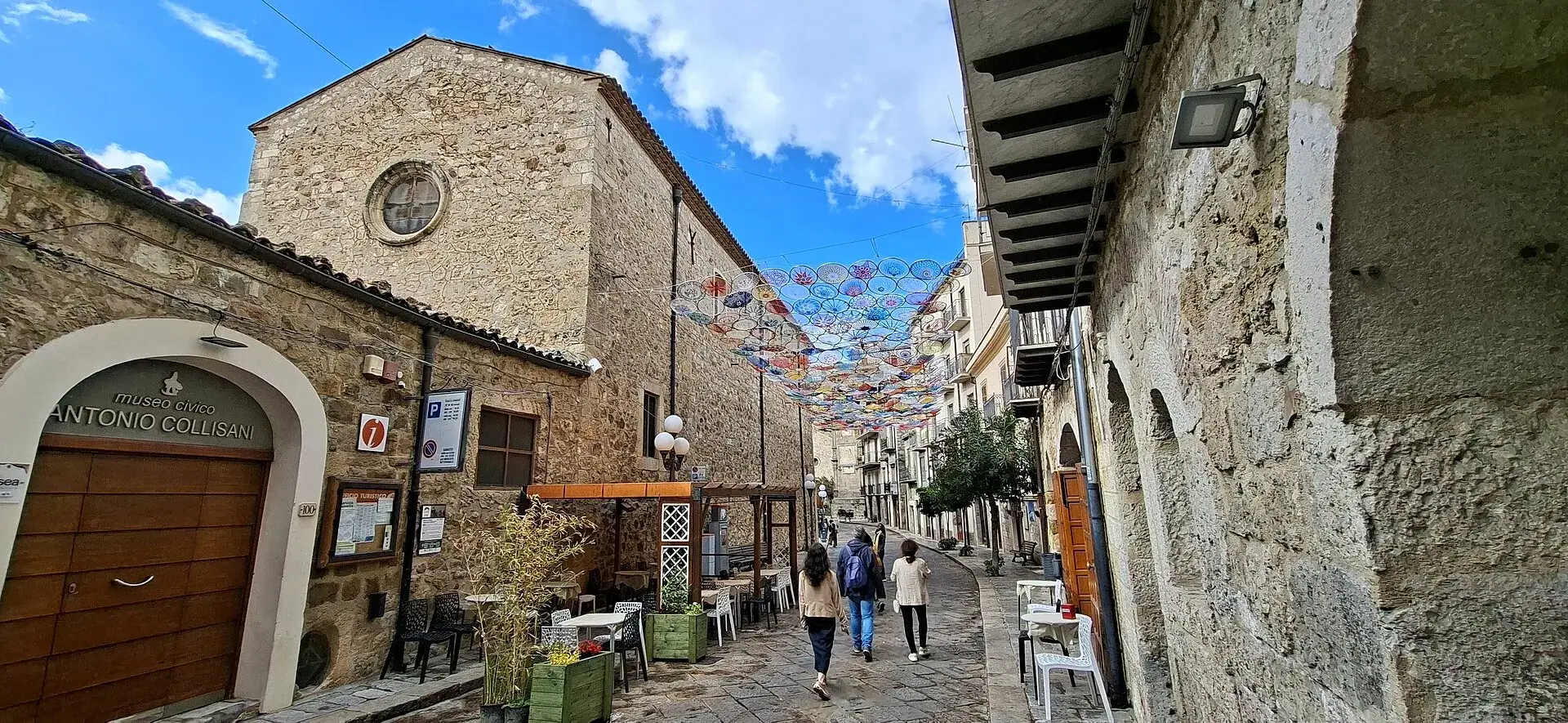 Corso di Petralia Sottana con ombrelli colorati appesi sopra la strada e facciate in pietra