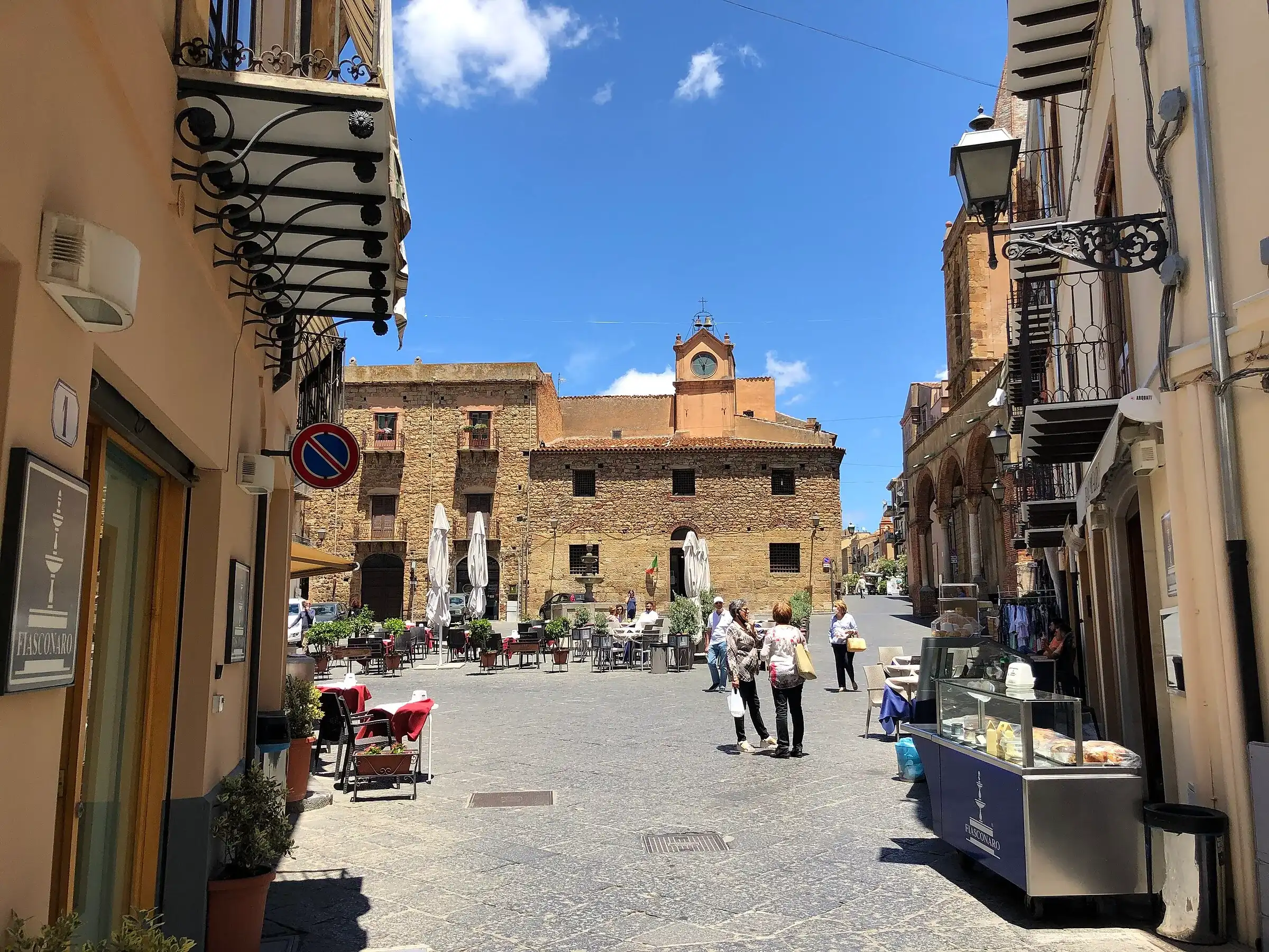 Una via del centro di Castelbuono che sbocca in piazza Margherita, con i tavolini e il palazzo con l’orologio