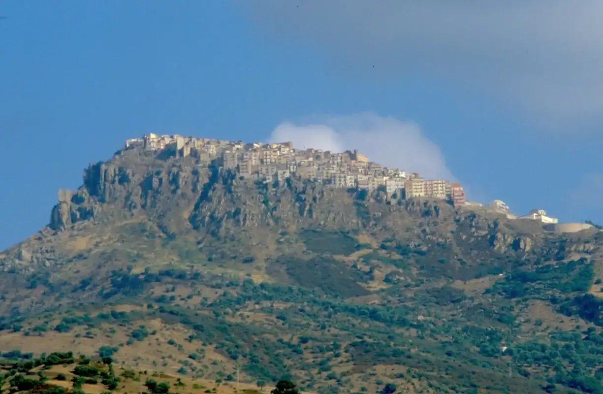 Pollina sulla sua rupe, vista dal basso oltre i pendii verdi