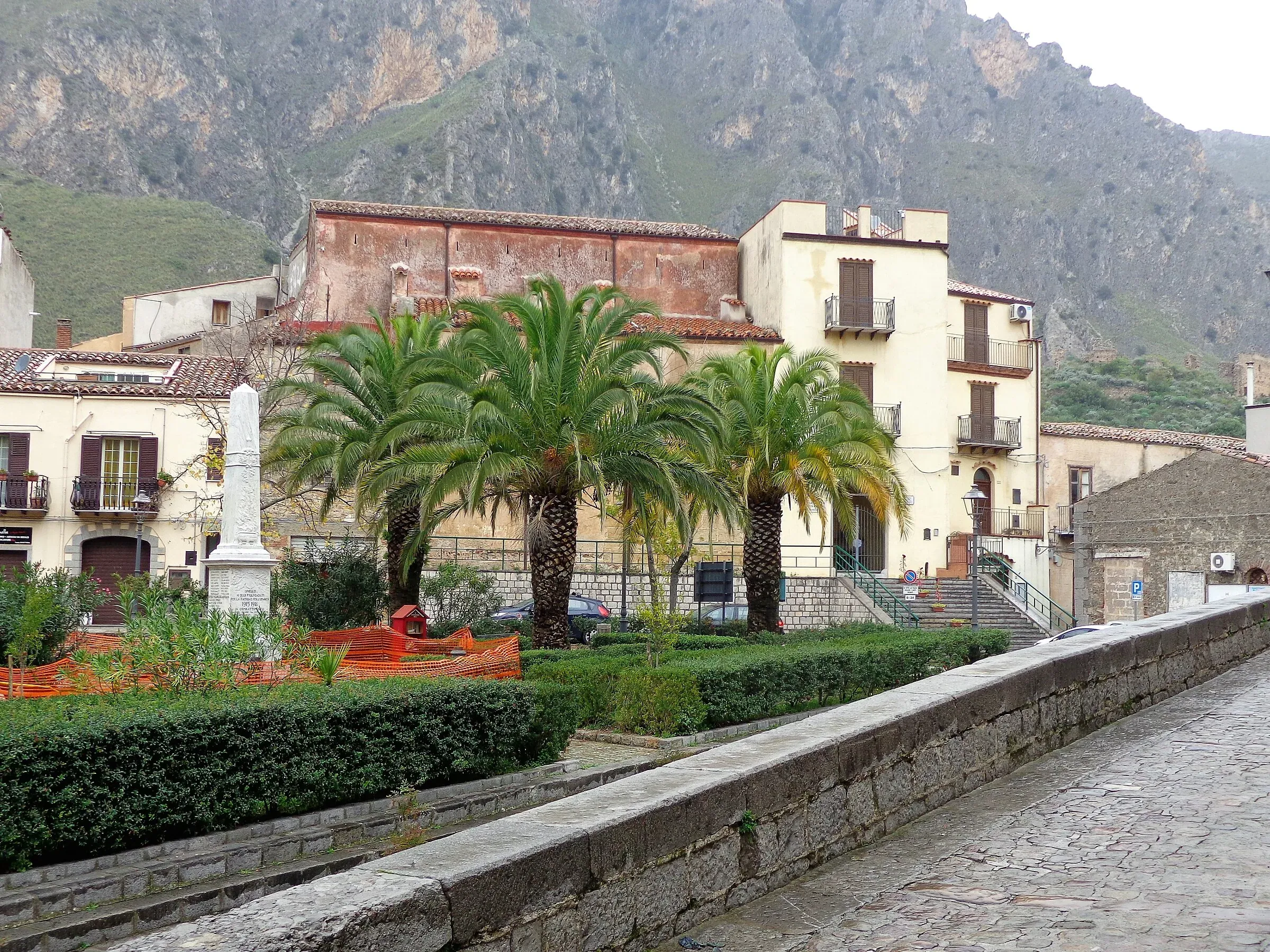 La chiesa della Madonna del Rosario e la piazza dei Caduti a Isnello, con le palme e i monti dietro