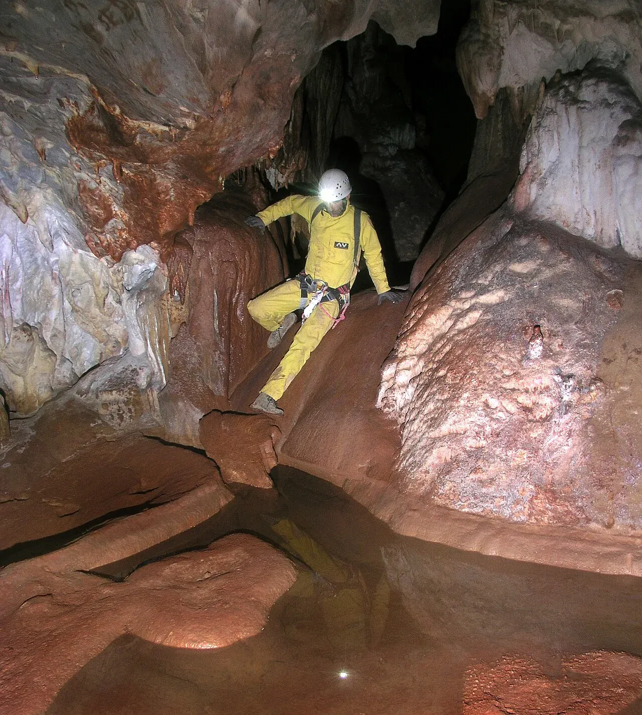 Speleologo in tuta gialla tra concrezioni e pozze d'acqua rossastra nella parte preistorica dell'Abisso del Vento, a Isnello